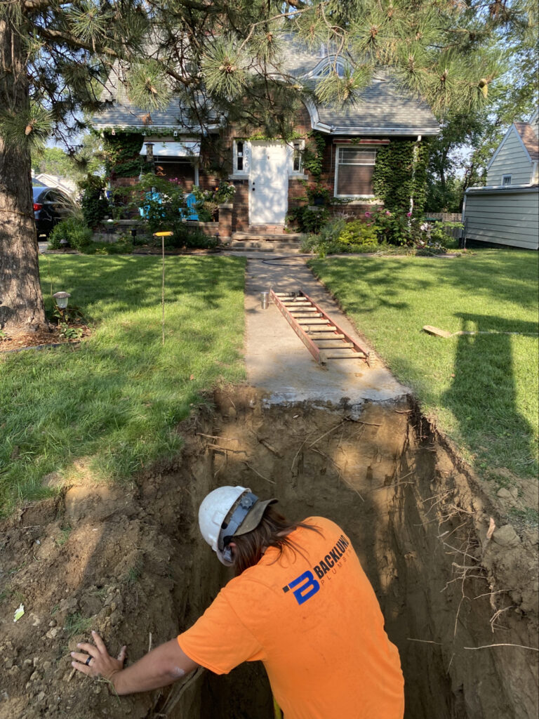 Worker in a hardhat stands in a hole outside a home.