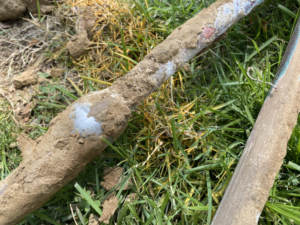 Two old lead service lines lay on the grass, covered in dirt.
