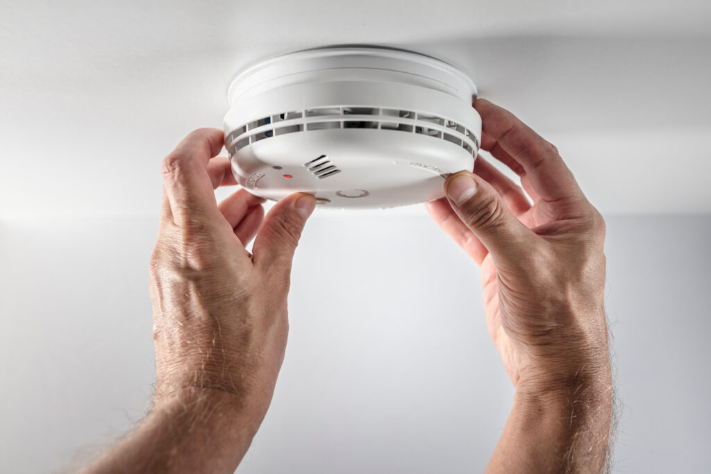 Close-up of hands securing a smoke alarm to a ceiling.