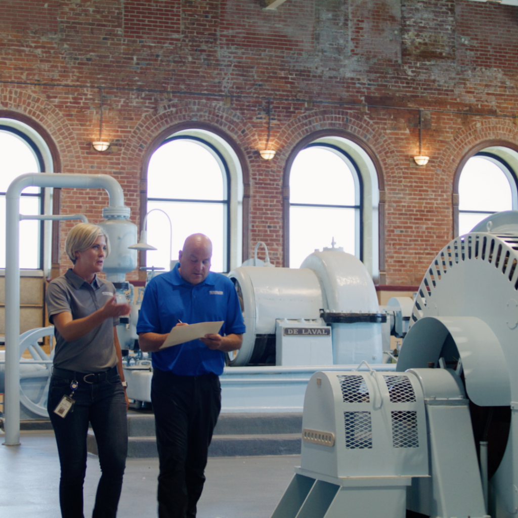 Two utility employees walk through Florence water treatment plant, reviewing documents beside large machinery
